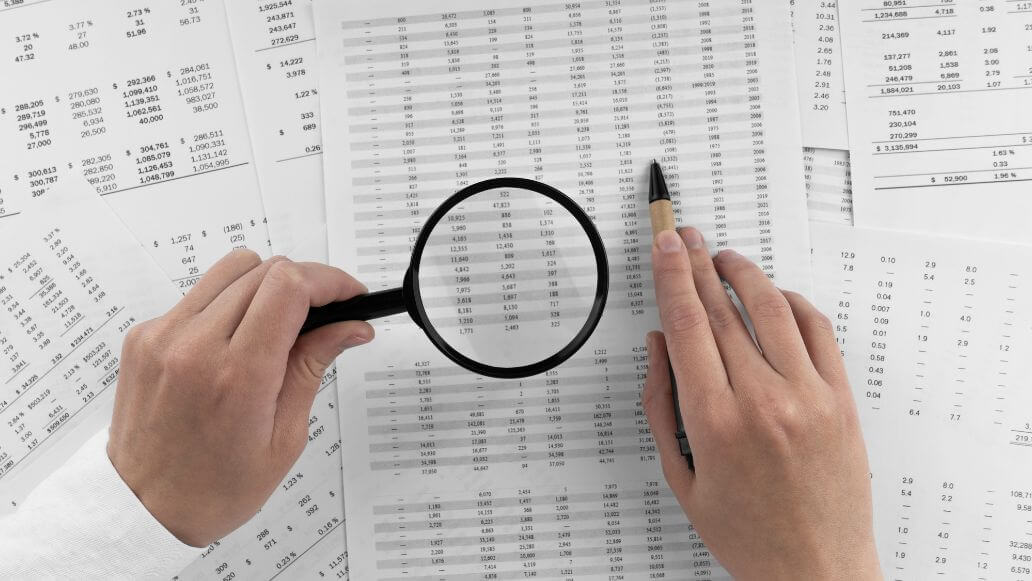 財務書類の数字を指す虫眼鏡を持つ女性