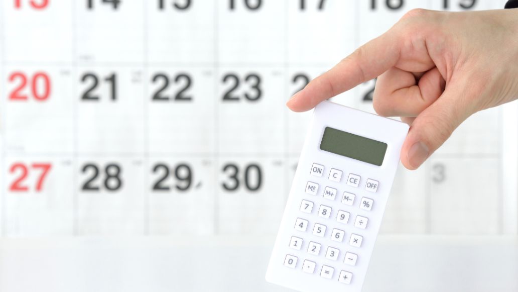 カレンダーの前で電卓を持つ人の手