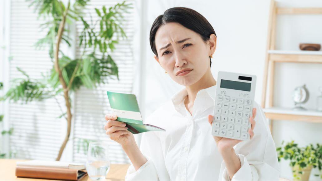銀行通帳と電卓を持ちながら思案する女性